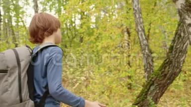 后景少年带背包走在秋公园的小路上。 少年男孩选择路上的岔路口